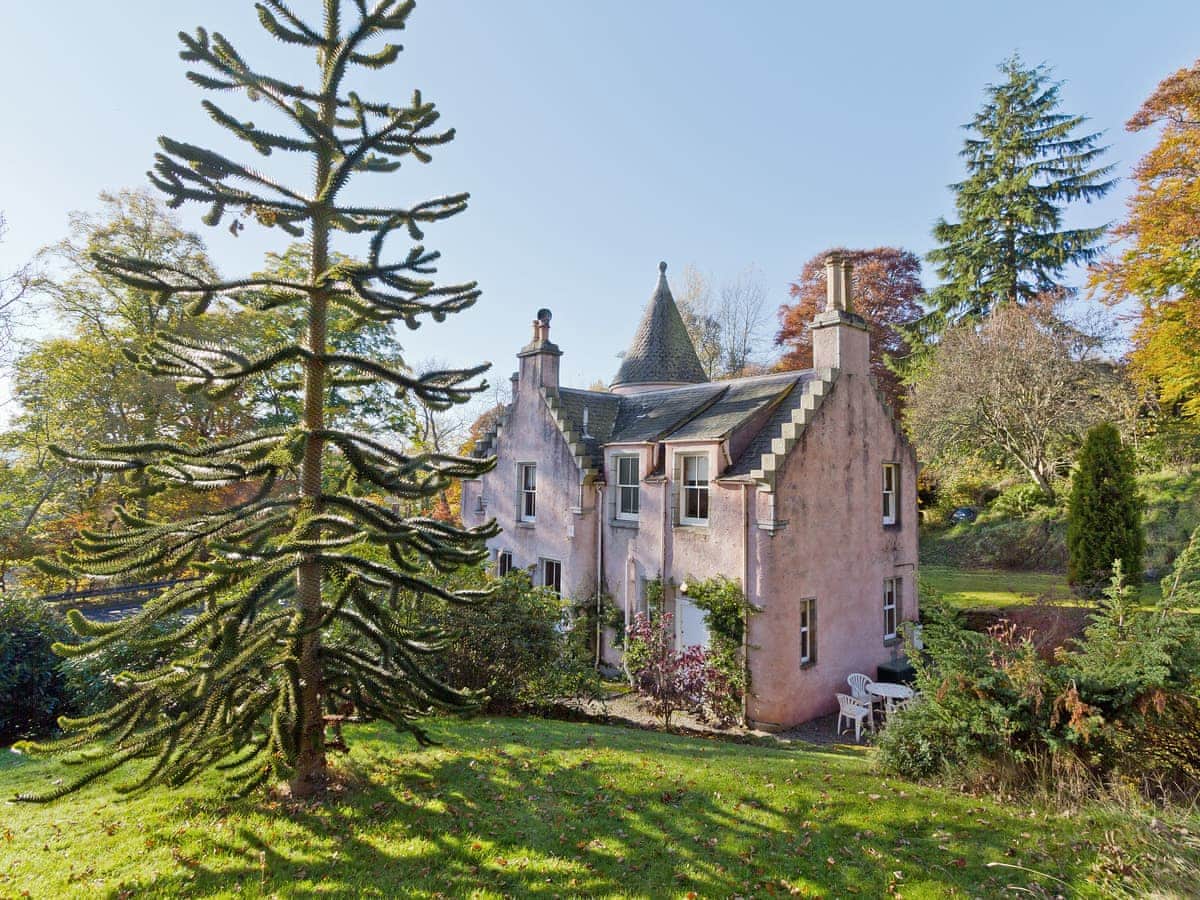 Victorian gatehouse with tower surrounded by trees with blue sky