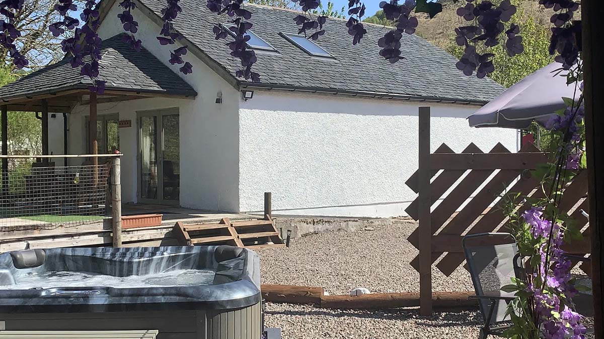 corner of a hot tub outside a white cottage