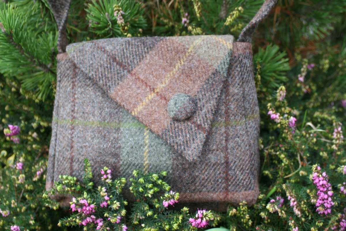 harris tweed handbag in brown and green sitting on a heather bush
